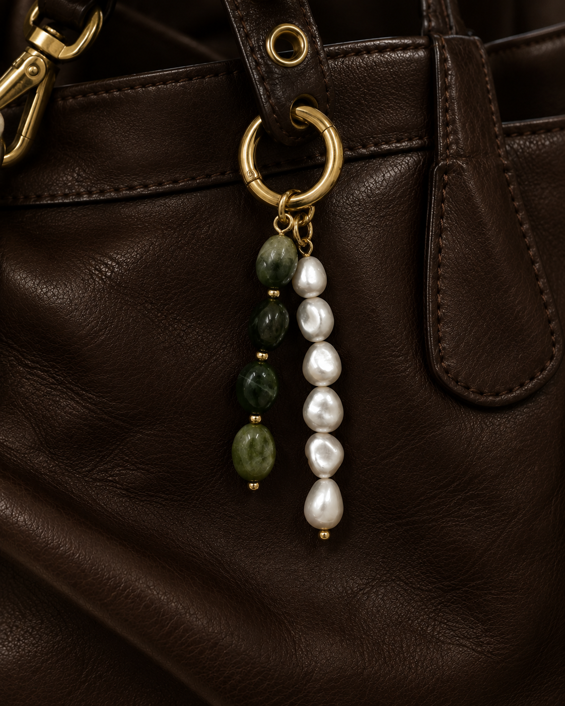 Folie à Trois Perla BAG CHARM in green jade and white pearl strands, hanging from a gold hoop clasp on a dark brown leather bag.