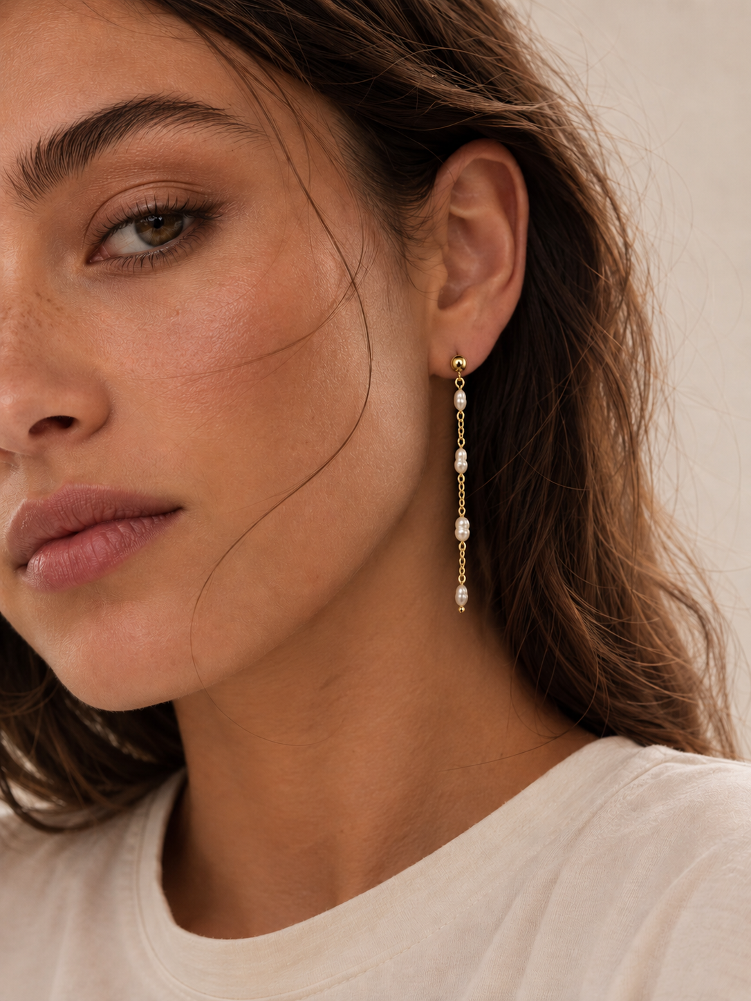 Close-up of a model wearing the gold Perla Luna EARRINGS, a long chain drop set with four pearls.