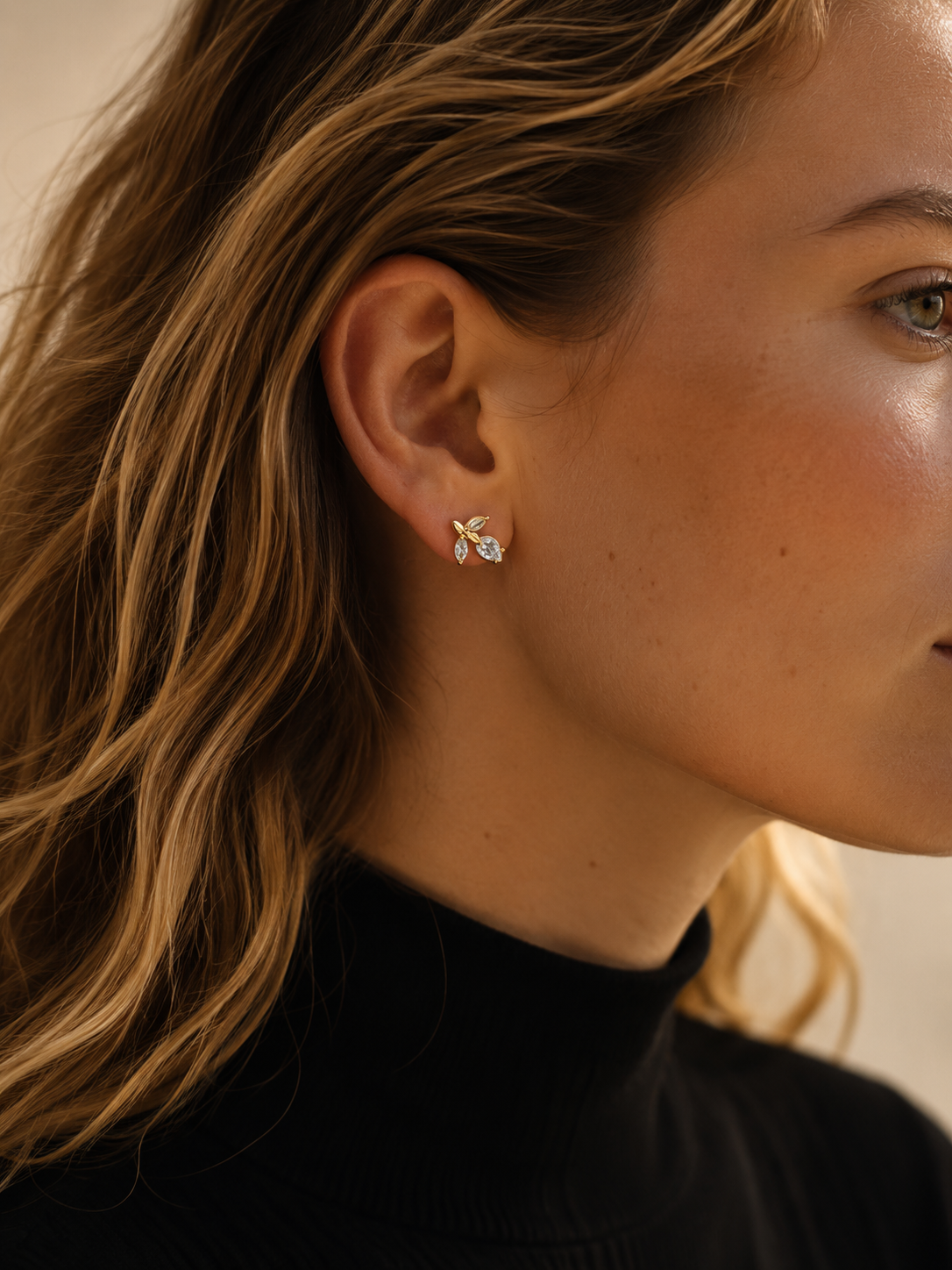 Close-up of a model in a black turtleneck wearing the gold Petiole EARRINGS, a vine-shaped stud set with zirconia leaves.