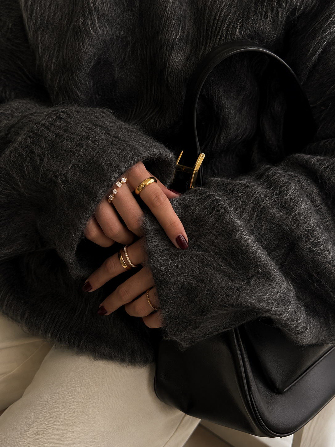 Model wears the gold Folie à Trois Pretty Thing RING stacked with several other gold rings on the hand, resting on a black leather bag.