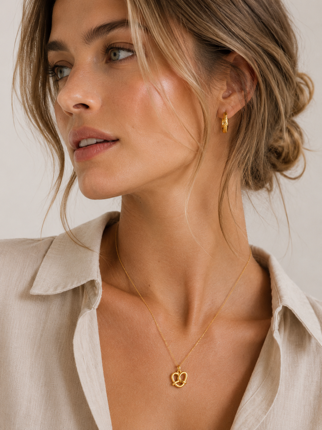 The Pretzel CHARM worn at the neckline with a matching gold hoop earring, the gold pretzel pendant on a fine chain.