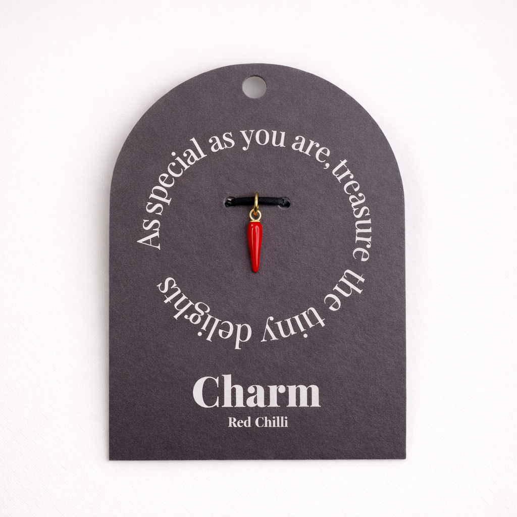 The Red Chili Pepper CHARM displayed on a charcoal Charm gift tag, the red enamel chili pendant hanging from a black cord.