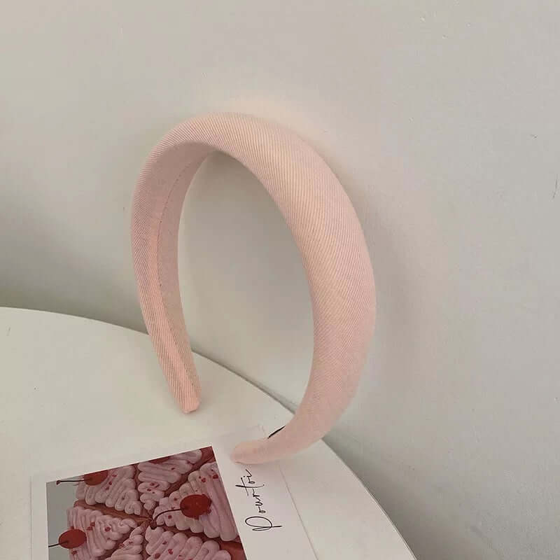 A single pale pink twill ribbed fabric padded headband styled upright near a small photo card.