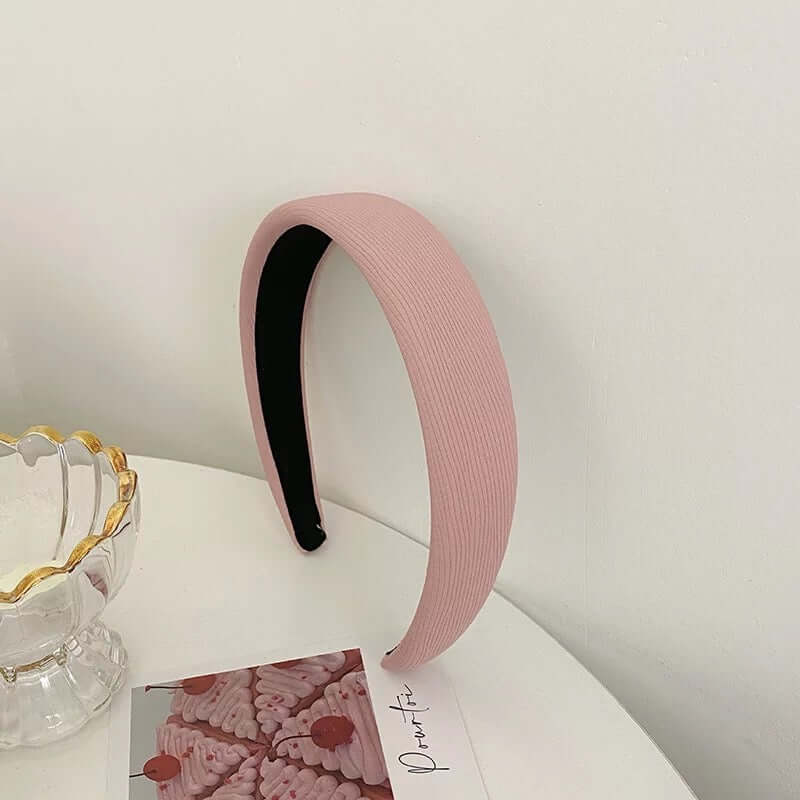 A single dusty rose ribbed fabric headband with black lining styled upright near a glass dish and photo card.
