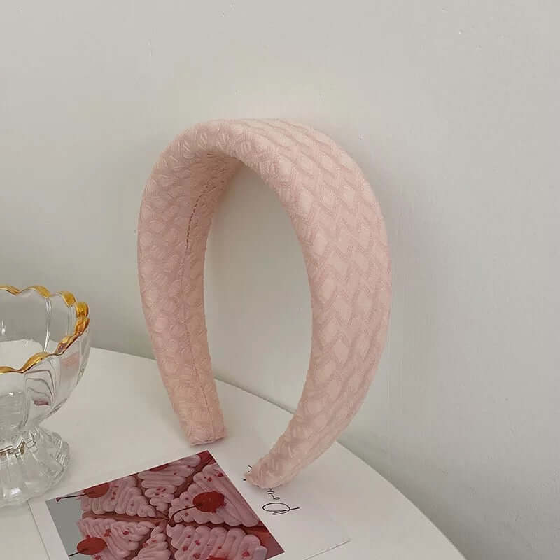 A single pale pink quilted textured padded headband styled upright near a glass dish and photo card.