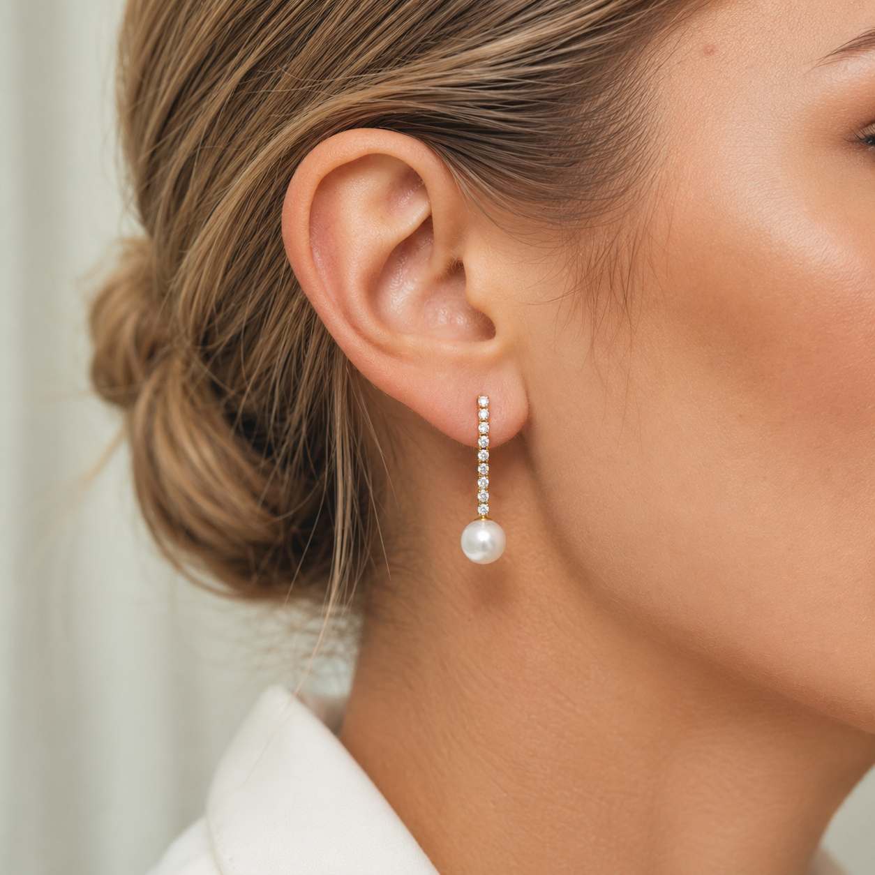 Rhea Earrings worn on the ear, a delicate crystal-lined chain trailing down from the lobe to a soft white pearl drop.