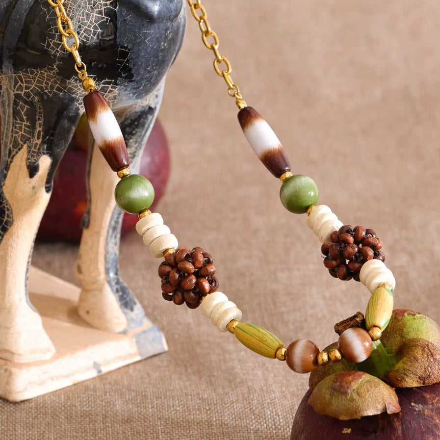 The Rio NECKLACE laid on woven fabric beside a mangosteen fruit, its striped agate and tiger's eye beads shown up close.
