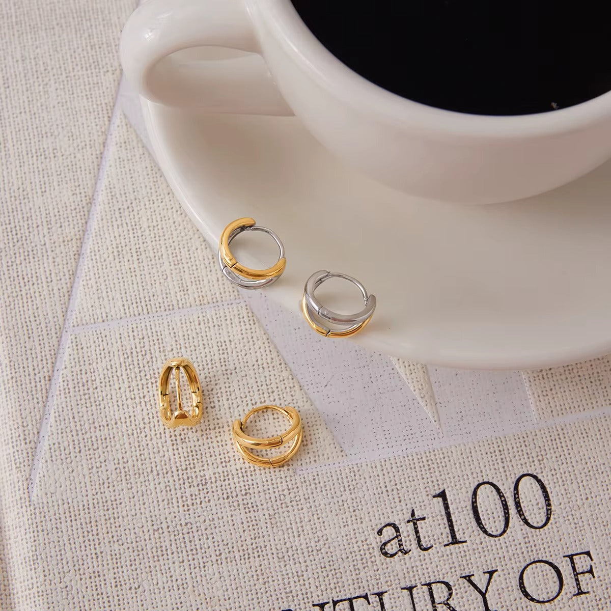 Close-up flat lay of Roadtrip Earrings on a book page next to a coffee cup, showing the chunky two-tone hoop design.