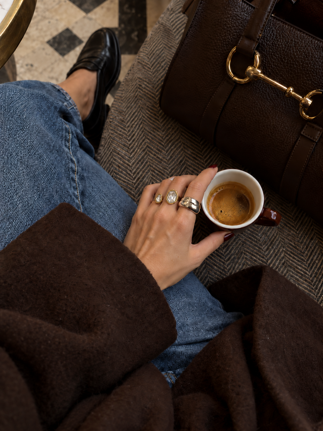 Hand holding an espresso cup at a café wears the gold Roche RING with zirconia among stacked rings — Folie à Trois wholesale