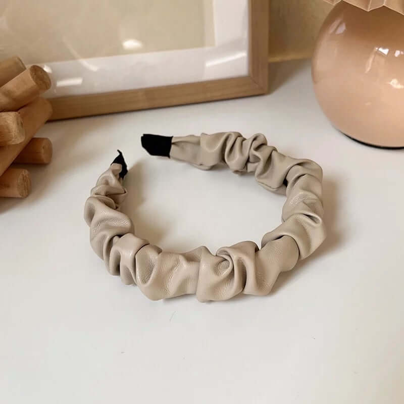 A single beige ruched faux leather Romy HAIRBAND laid flat on a white surface, showing its knotted ruched texture in detail.