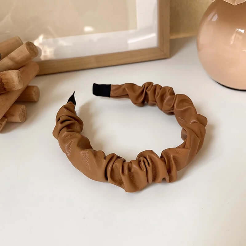 A single camel tan ruched faux leather Romy HAIRBAND laid flat on a white surface, showing its knotted ruched texture in detail.
