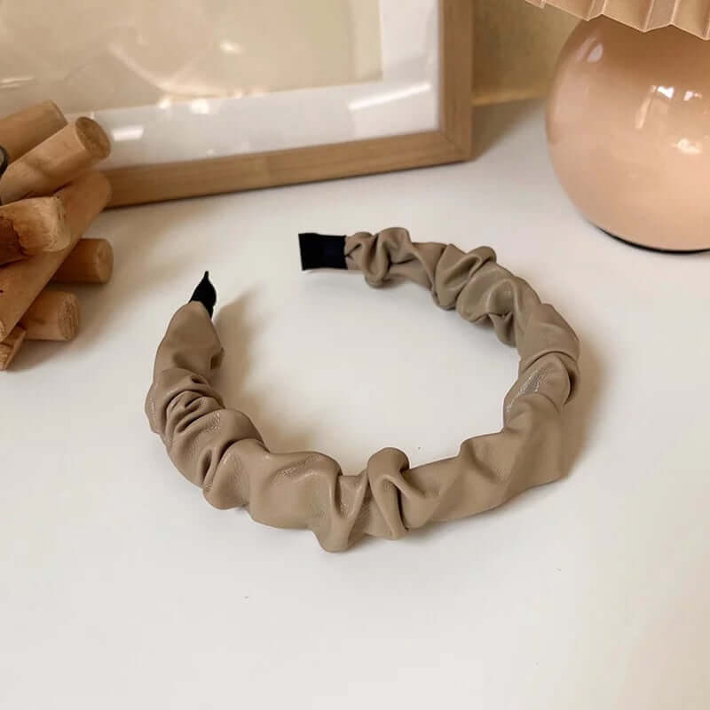Close-up of a beige ruched faux leather Romy HAIRBAND laid flat, highlighting its knotted texture and matte leather finish.