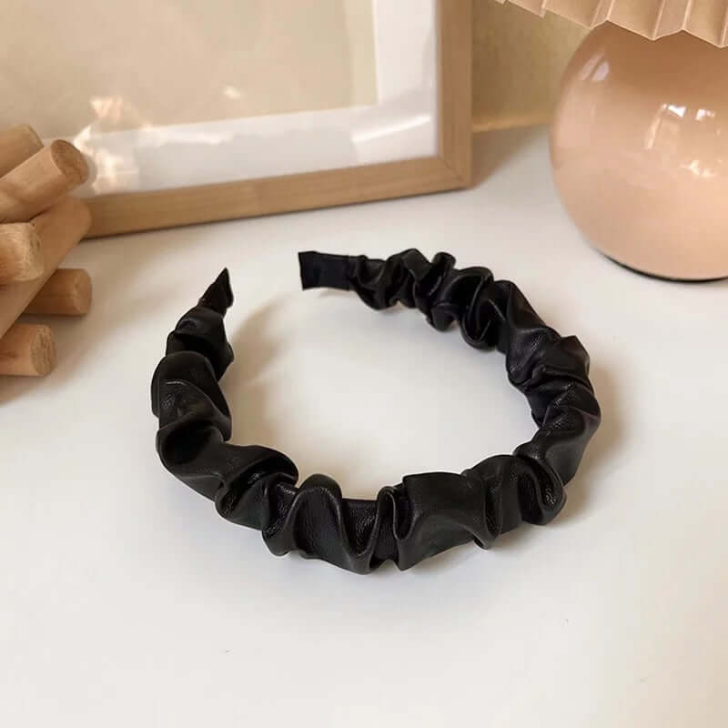 A single black ruched faux leather Romy HAIRBAND laid flat on a white surface, showing its knotted ruched texture in detail.