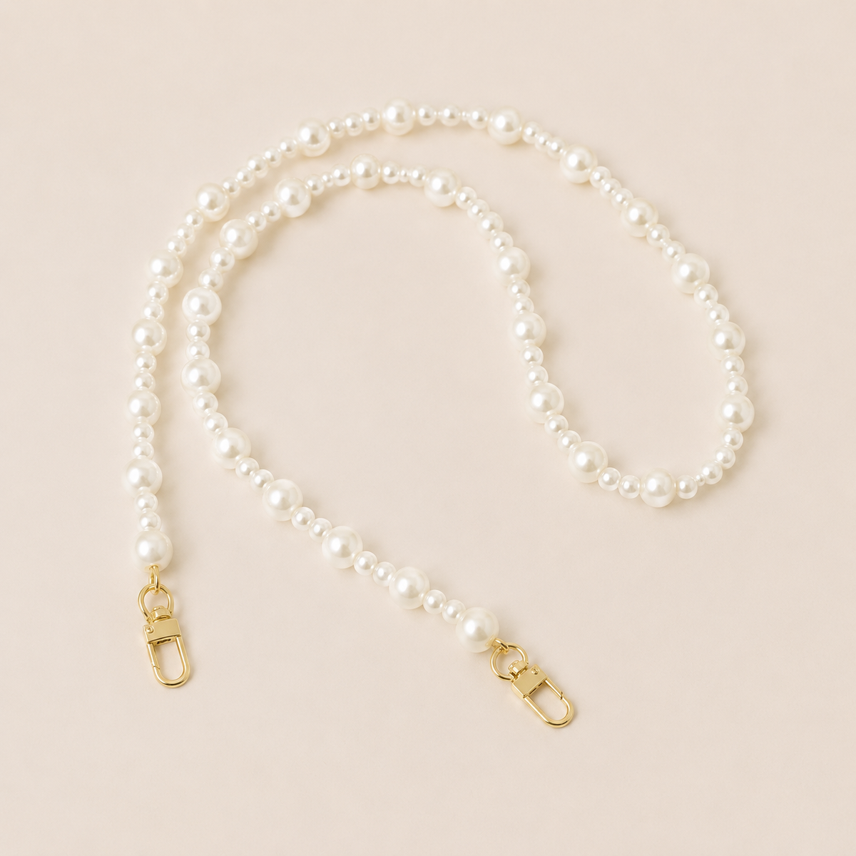 Folie à Trois Sabine Pearl long phone chain in graduated white faux pearls with gold clasps, coiled on a cream background.