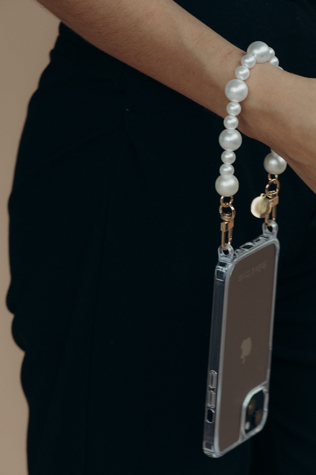 Close-up of the Folie à Trois Sabine Pearl wholesale phone chain wrapped around a wrist and attached to a clear phone case with gold clasps.