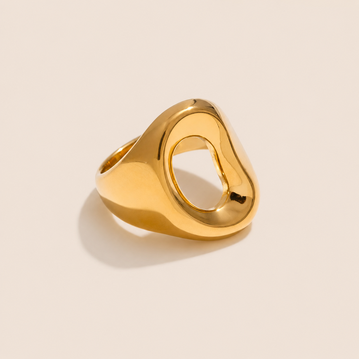 Gold chunky signet ring with an organic, asymmetric open oval cutout, shown on a cream backdrop — Folie à Trois Salt Air RING.