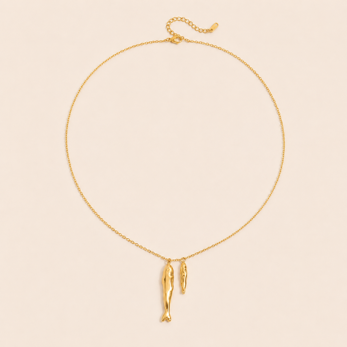 Gold Sardina NECKLACE with two fish charms and an adjustable clasp, shown fastened in a circle on a beige background.