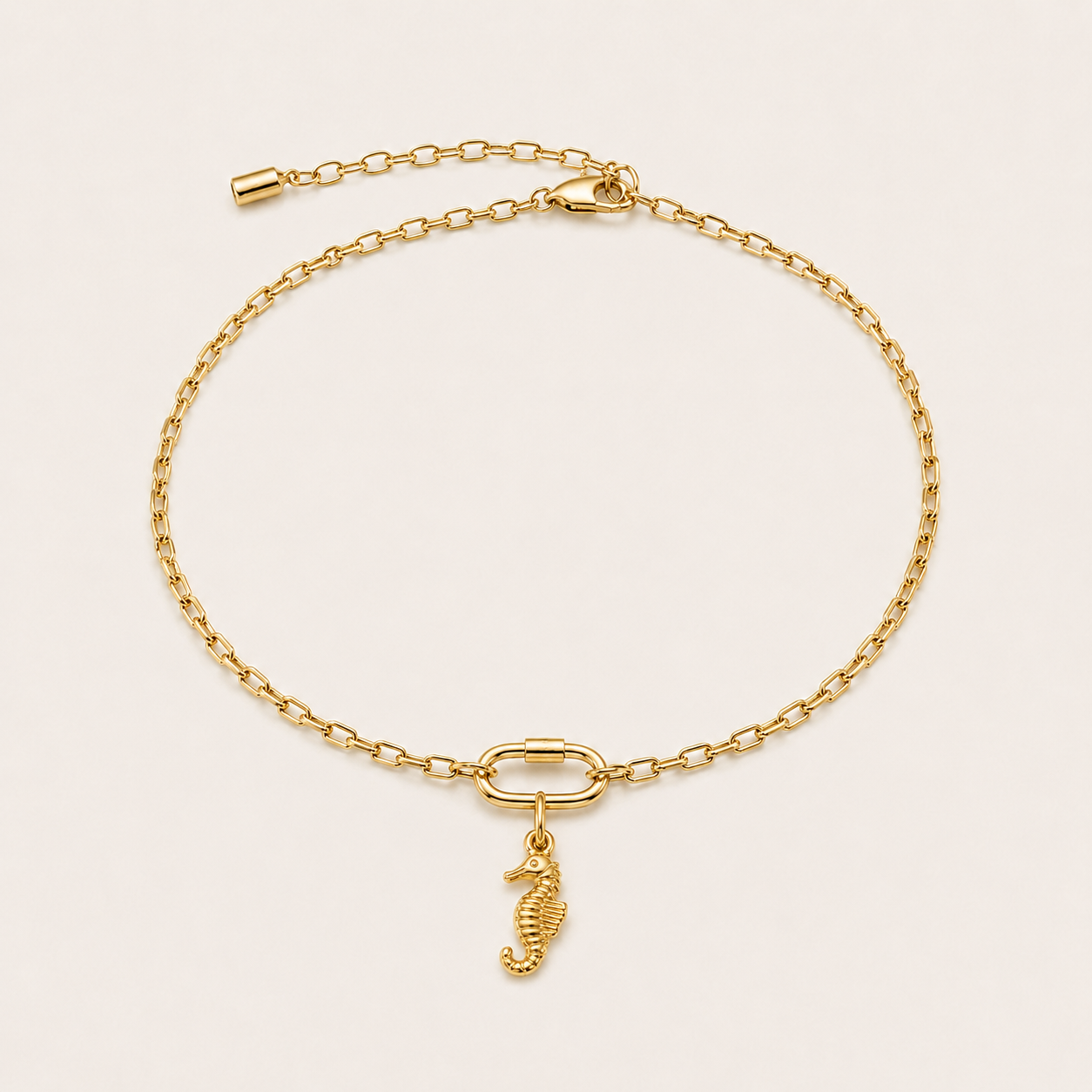 The Seahorse CHARM worn as a charm on a gold paperclip-link anklet with an oval carabiner clasp, shown flat on cream.