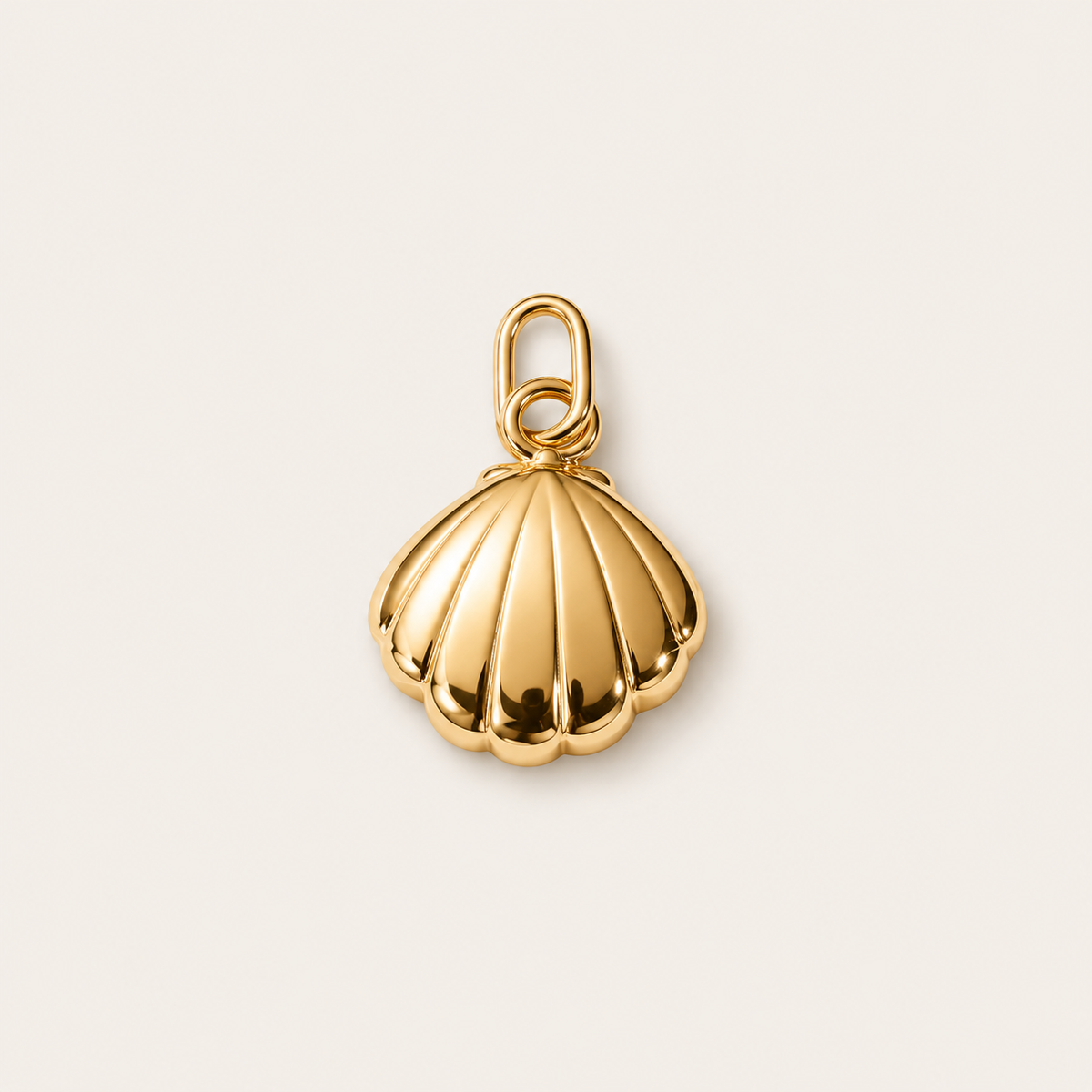 The Shell CHARM in gold, a scalloped clam shell pendant with a ribbed texture, shown in close-up studio photography on cream.