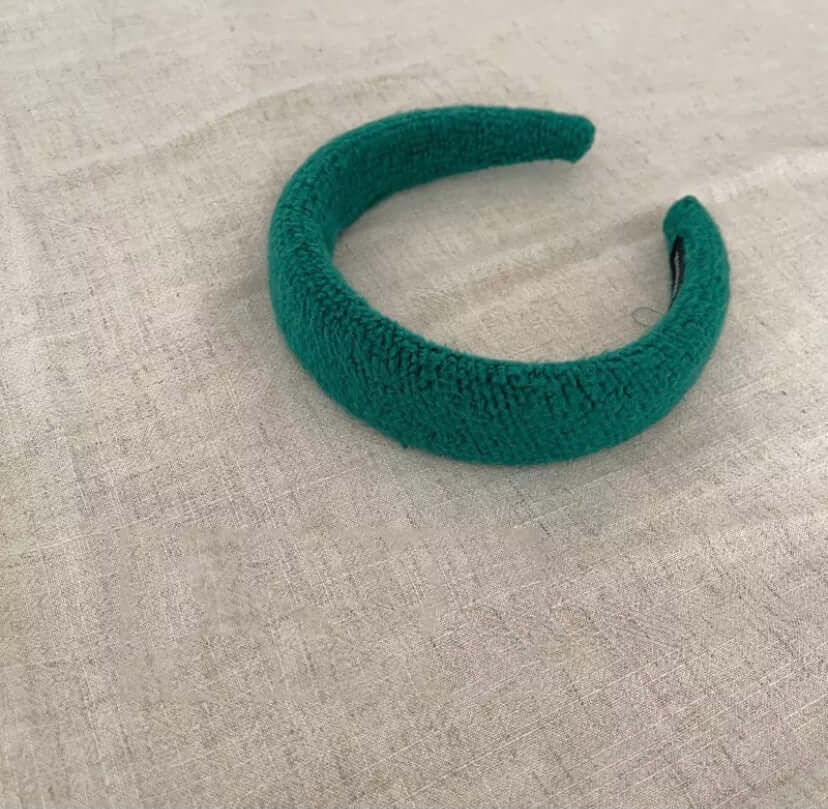 A single teal green boucle padded Skylar HAIRBAND laid on linen fabric.