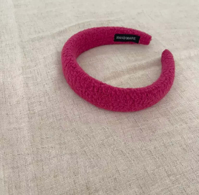 A single magenta pink boucle padded Skylar HAIRBAND with a handmade label tag, laid on linen fabric.