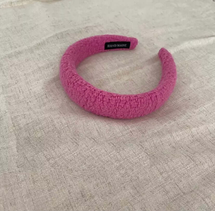 A single rose pink boucle padded Skylar HAIRBAND with a handmade label tag, laid on linen fabric.