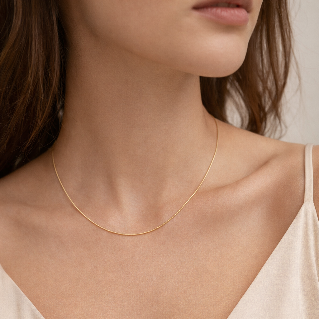 The Small Snake Charm NECKLACE worn close-up at the neckline, its slim gold snake chain resting against bare skin.