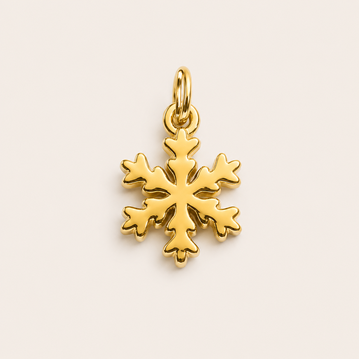 The Snowflake CHARM in gold, a detailed snowflake pendant with a jump ring, shown in close-up studio photography on cream.