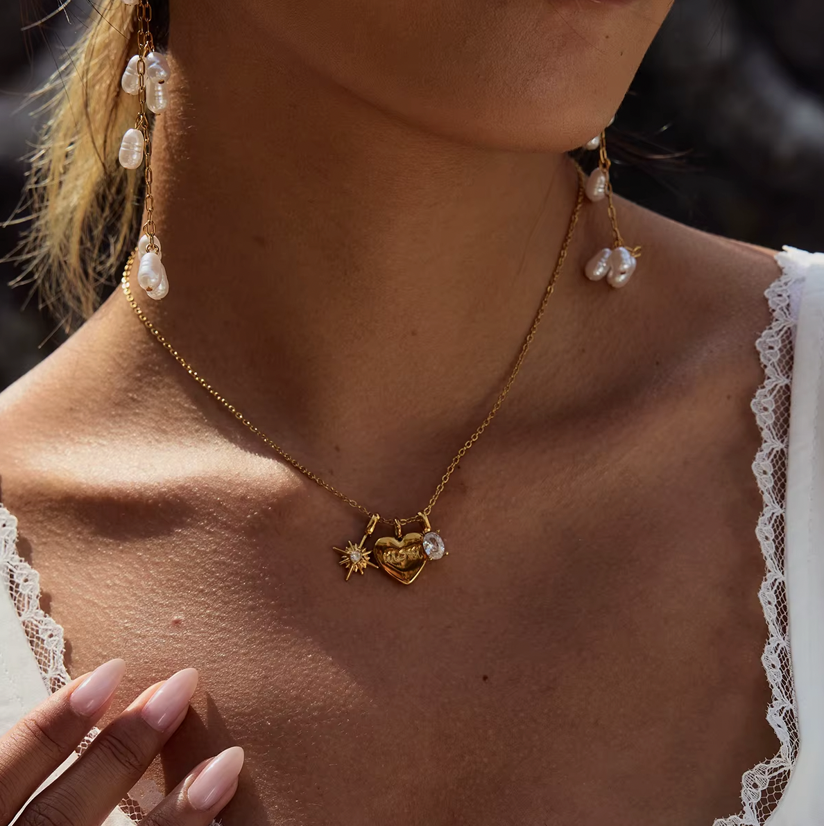The Soft Power NECKLACE worn close-up with dangling pearl drop earrings, styled with a lace-trimmed top and hand on the chest.