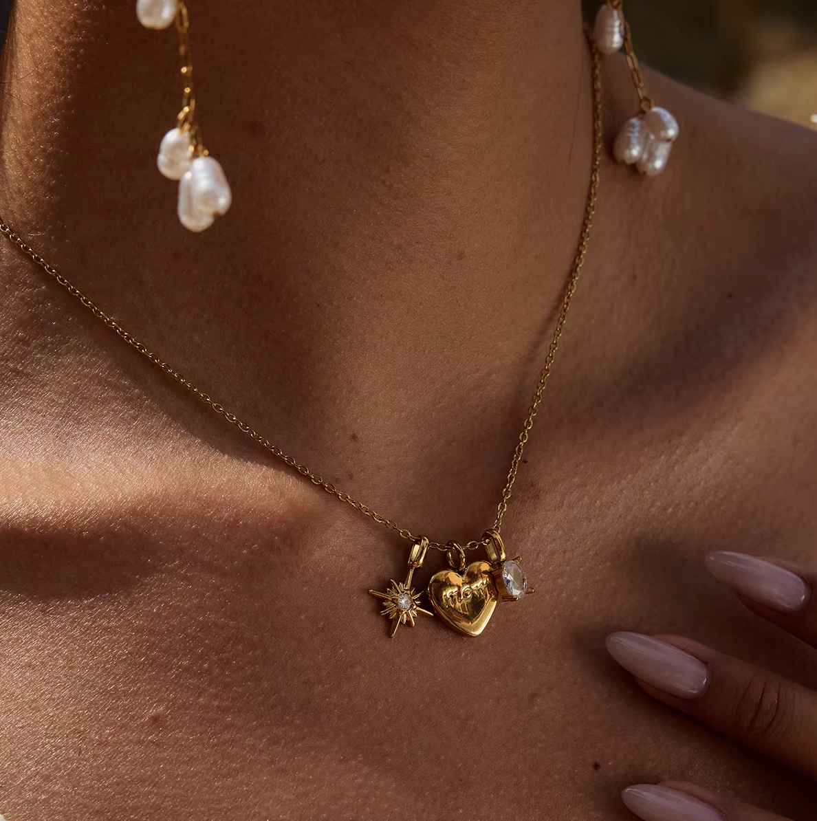 The Soft Power NECKLACE worn in tight close-up, its charms and pearl earrings sharp as the model's ringed fingers rest nearby.