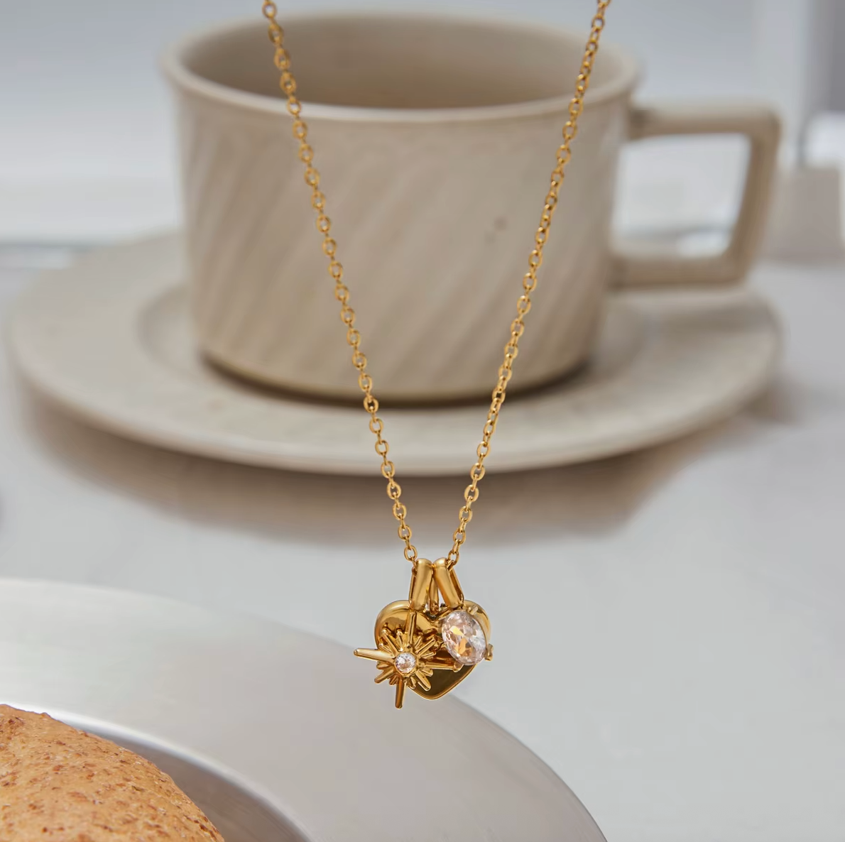 The Soft Power NECKLACE hanging in front of a teacup and saucer, its star, heart, and crystal charms in close focus.