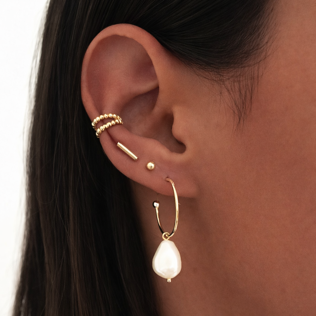 The Solara EAR CUFF worn on the ear cartilage, a beaded gold cuff layered above a pearl drop hoop earring stack.