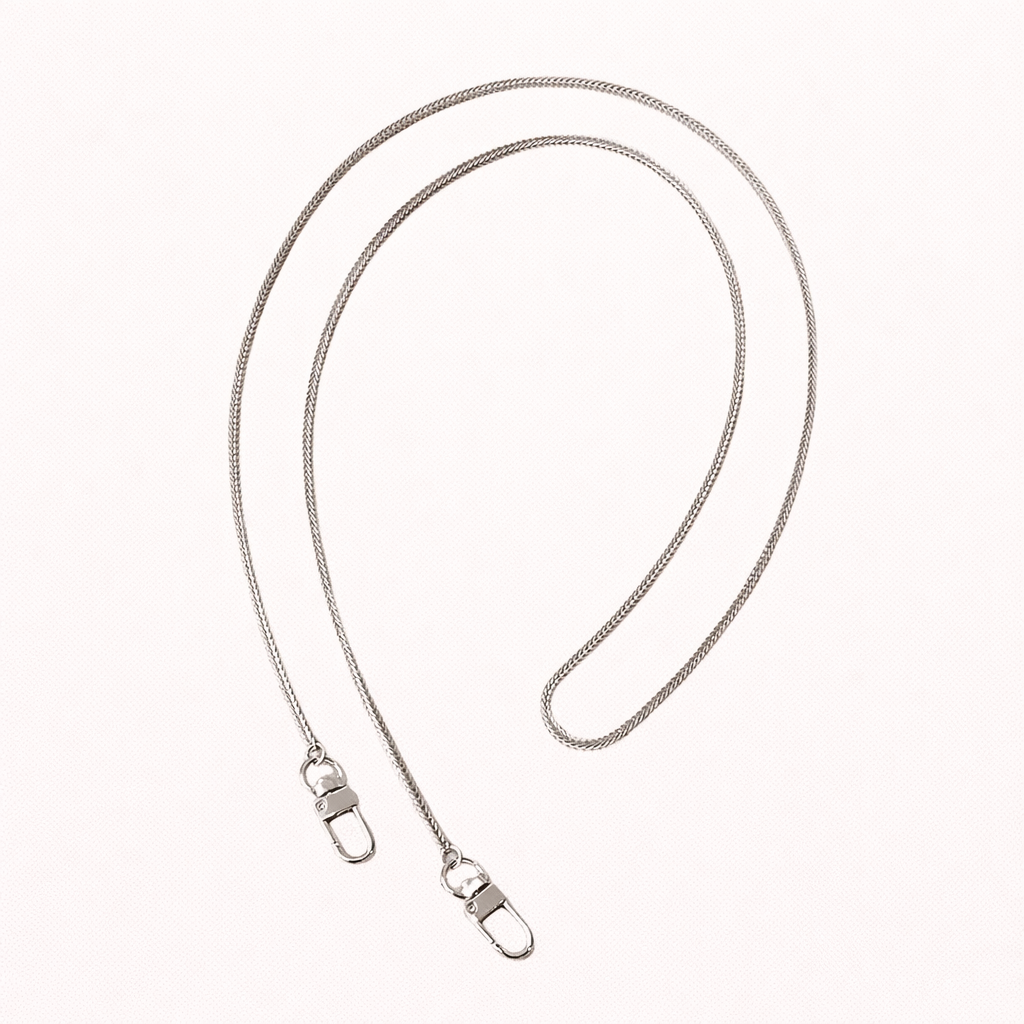 Delicate silver snake-chain phone strap coiled flat, mirroring the gold version with matching lobster clasps.