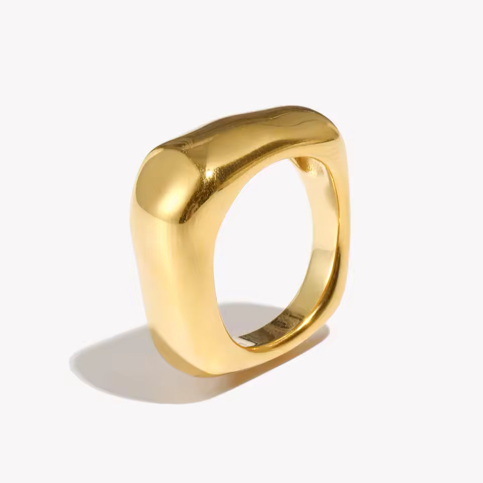 Chunky gold ring with a smooth rounded squared-off band and domed top, shown at an angle on a cream backdrop — Square Up RING.