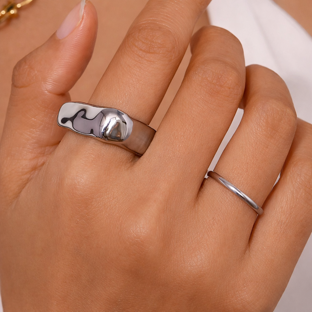 Close-up of a hand wearing a chunky black-and-white patterned ring with a domed silver accent, paired with a thin plain band.