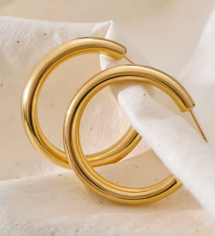 Statement Hoop earrings styled on a soft white fabric, showing the thick polished gold tube up close.