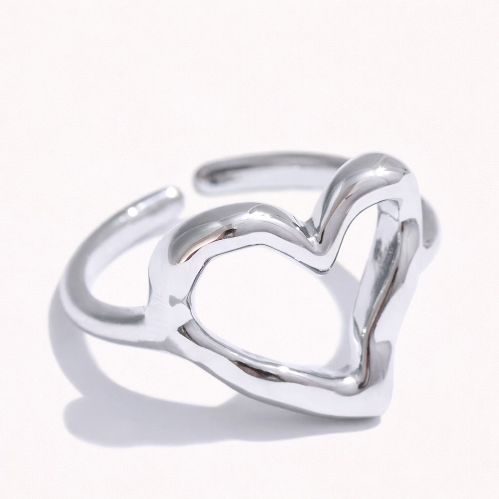 Open silver ring shaped like an outlined heart, shown at an angle on a cream backdrop — Folie à Trois Street Side RING.