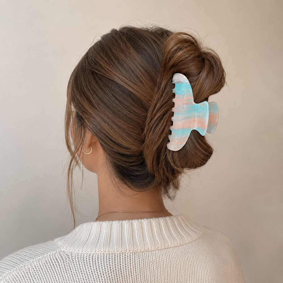 Sundae HAIR CLIP in a pastel blue and peach marbled pattern, worn holding a low bun on brunette hair.