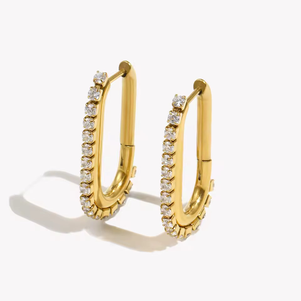 Sweet Thing Earrings in gold, an oblong paperclip-shaped hoop lined with crystals along one edge, shown as a pair.