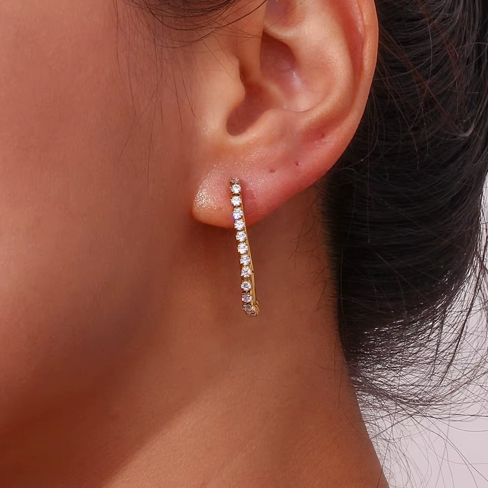 Close-up of a Sweet Thing Earring worn on the ear in gold, the crystal-lined oblong hoop hanging down.