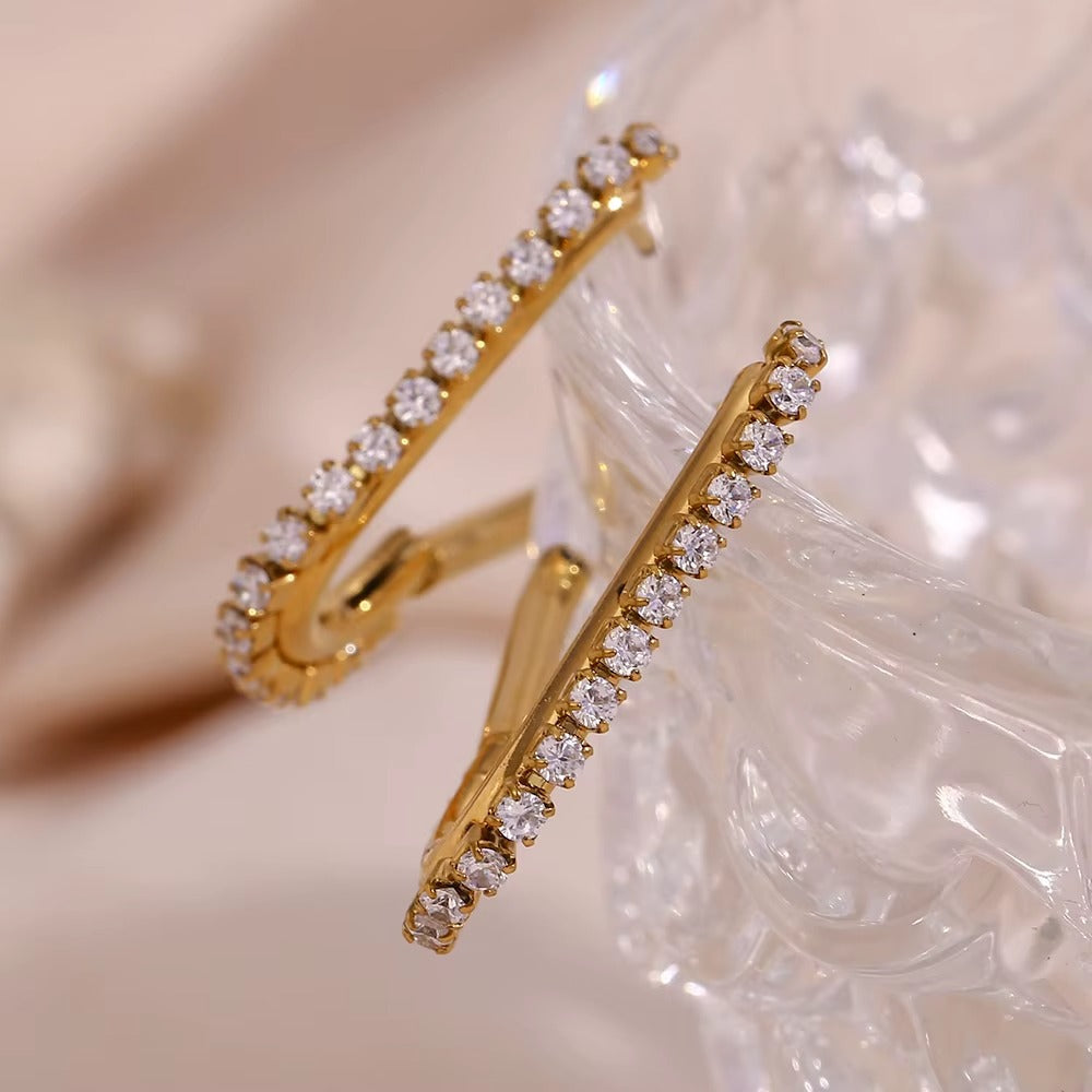 Macro shot of Sweet Thing Earrings in gold resting on a glass dish, the crystal-lined edges sparkling.