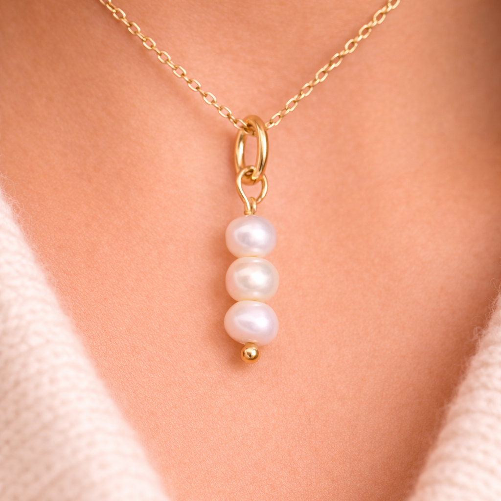 The Sweet Water Pearls CHARM worn at the neckline, three stacked freshwater pearls hanging from a gold paperclip chain.