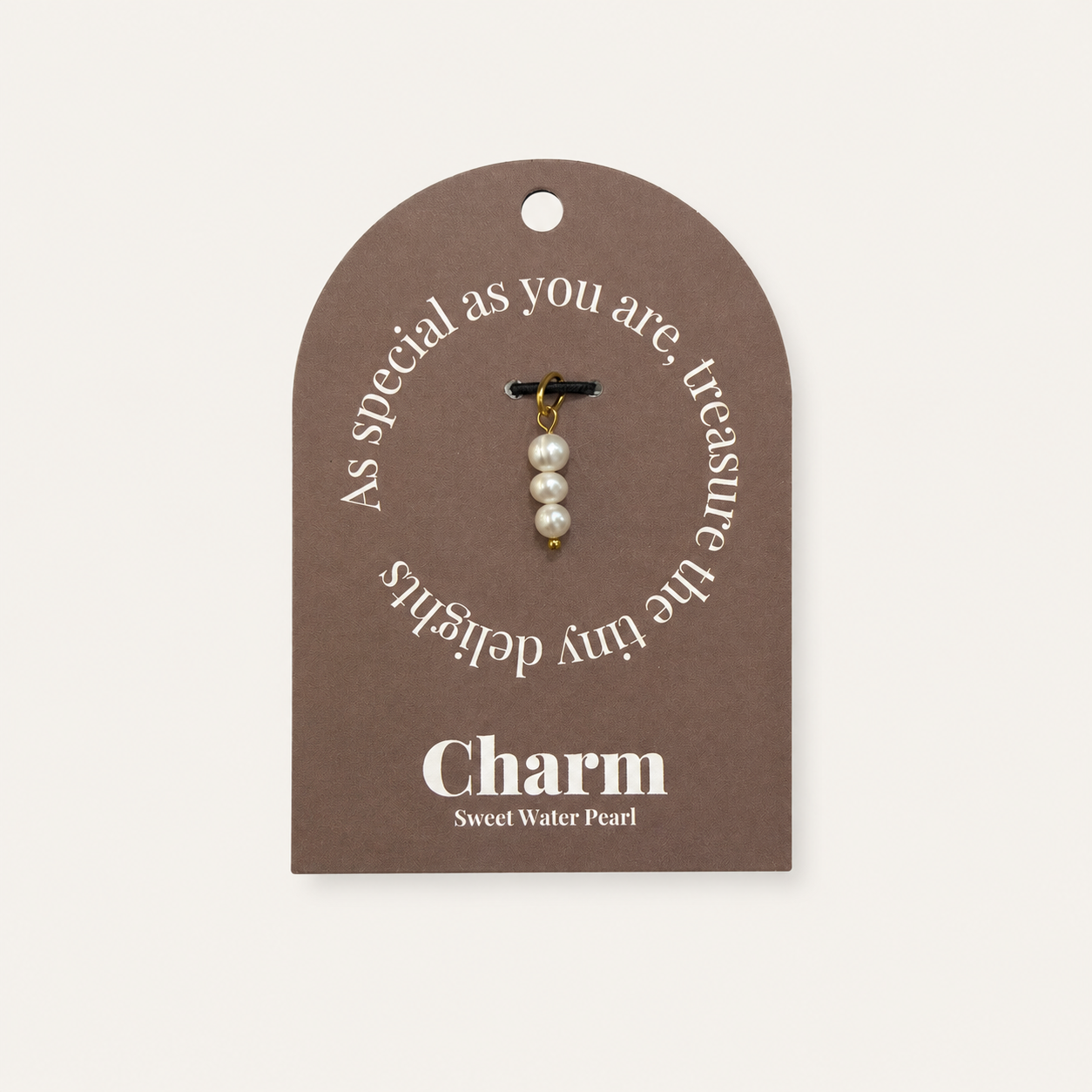 The Sweet Water Pearls CHARM displayed on a brown Charm gift tag, three stacked pearls hanging from a black cord.