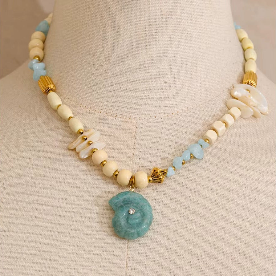 The Tahiti NECKLACE displayed on a mannequin bust, its cream beads and carved shell pendant shown in close, detailed focus.
