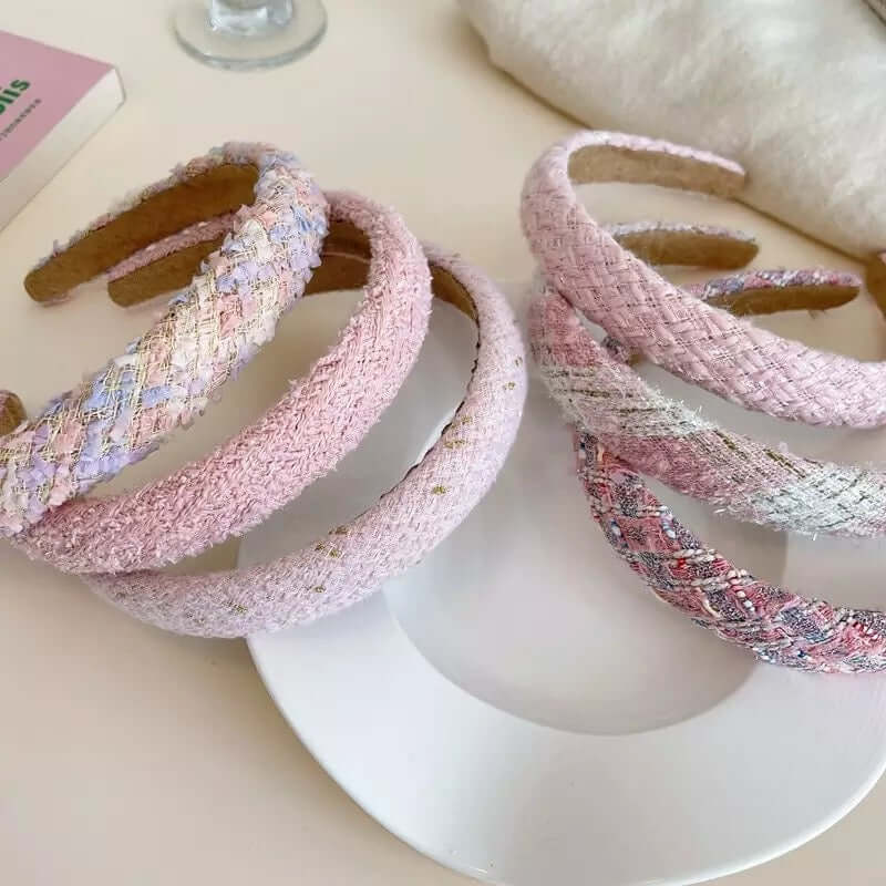 Six pink-toned tweed and boucle headbands in different patterns grouped together on a white plate.