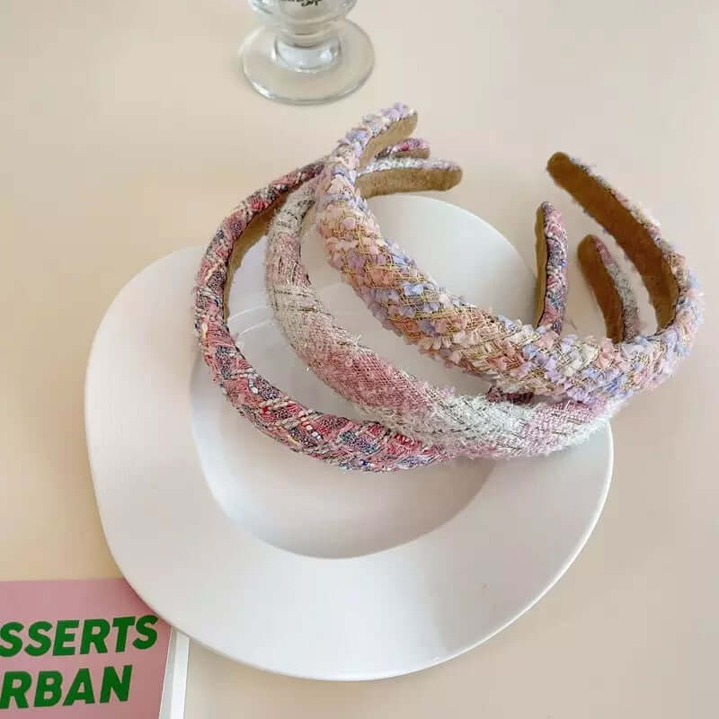 Four pink-toned tweed headbands in different patterns, including a fleck weave and solid boucle, grouped on a plate.