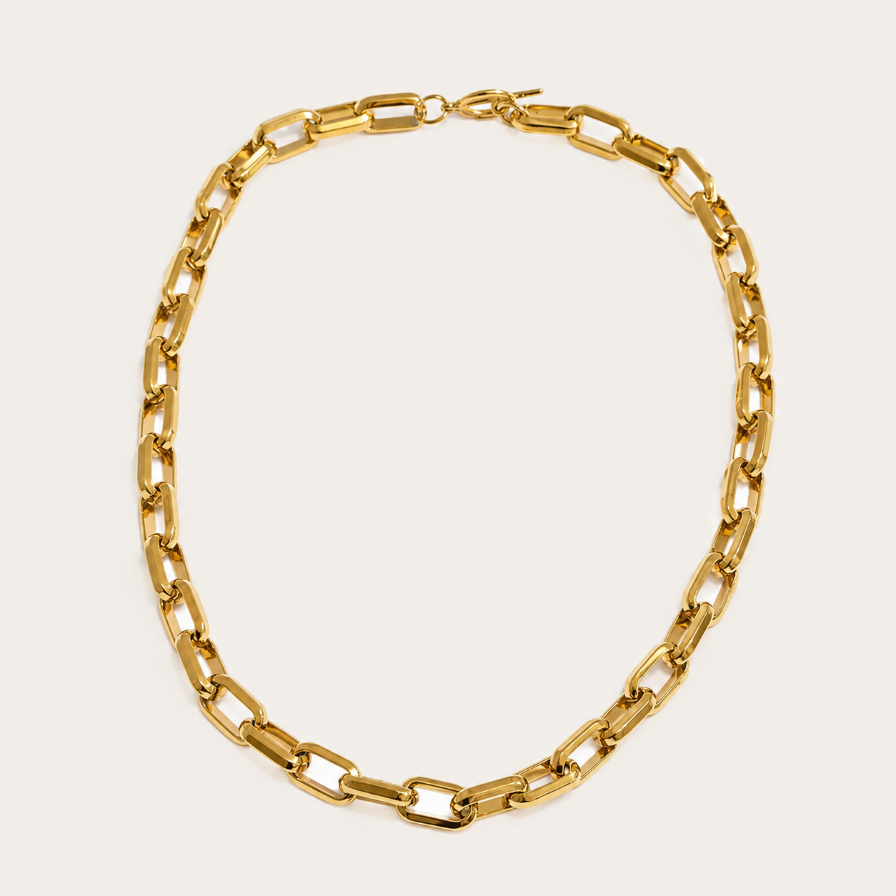 Gold chunky chain necklace with rectangular links from the Resort Edit NECKLACE design, laid flat on a beige background.