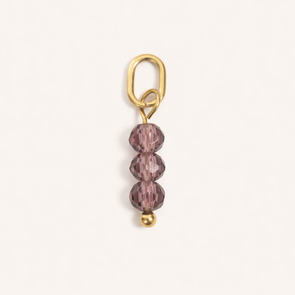 The Three Beads CHARM in a flat lay, three faceted mauve glass beads stacked above a gold ball on a gold paperclip-style connector.