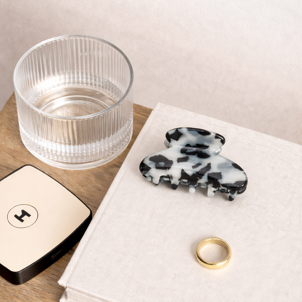 The Till Sun Up HAIR CLIP styled flat lay on a book beside a ribbed glass, a gold ring and a compact mirror.