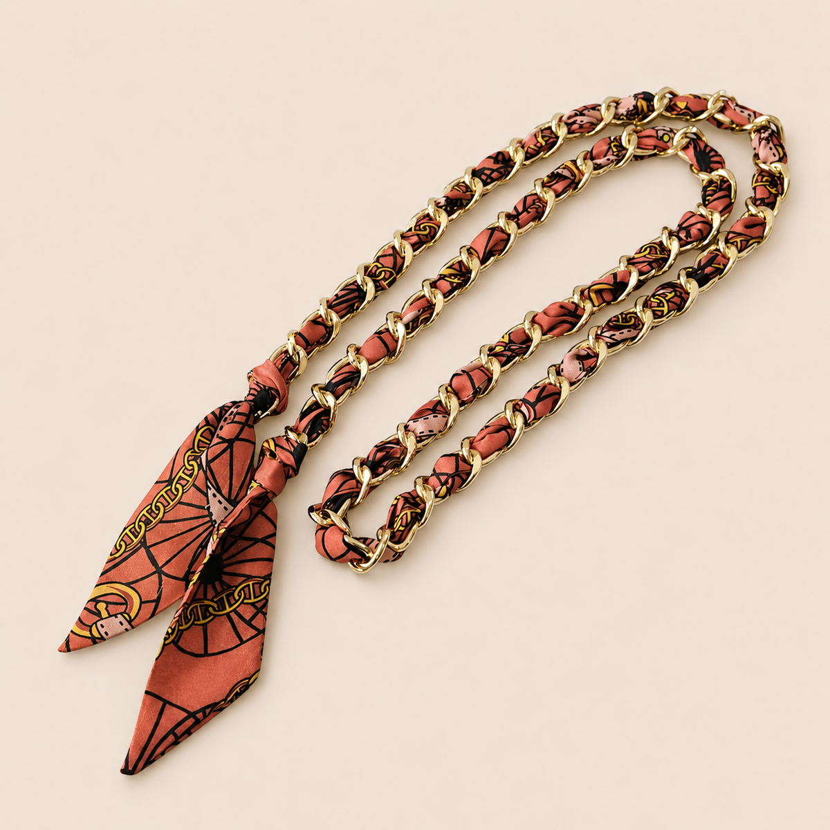 Terracotta printed silk scarf woven through a gold chain-link Tossa phone chain, tied in a knot.